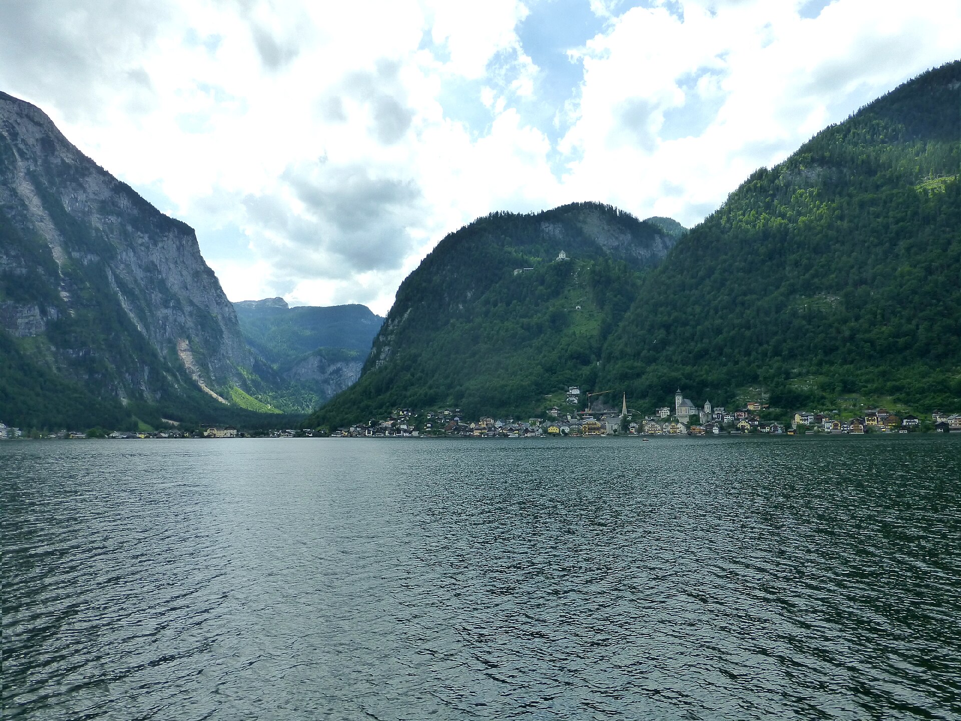 El lago de Hallstatt encajonado entre laderas boscosas, con el pueblo a la orilla.