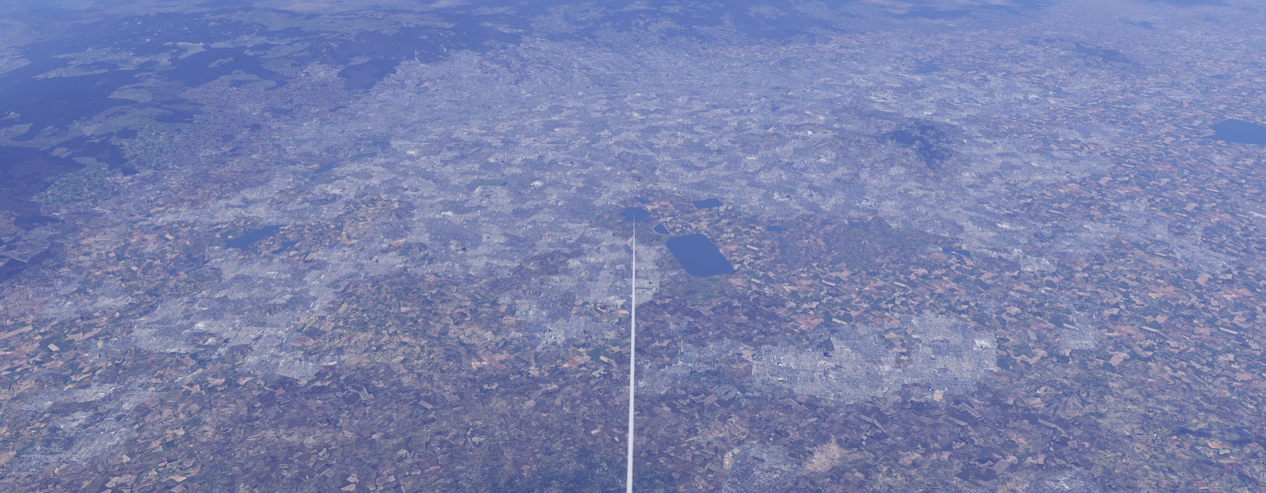 Vista oblicua de una llanura urbanizada casi por completo, con varios cuerpos de agua oscuros en el centro, uno grande y rectangular, y sierras boscosas al fondo.